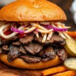 A beef brisket sandwich with coleslaw and BBQ sauce on a wooden board, accompanied by pickles and dipping sauce.